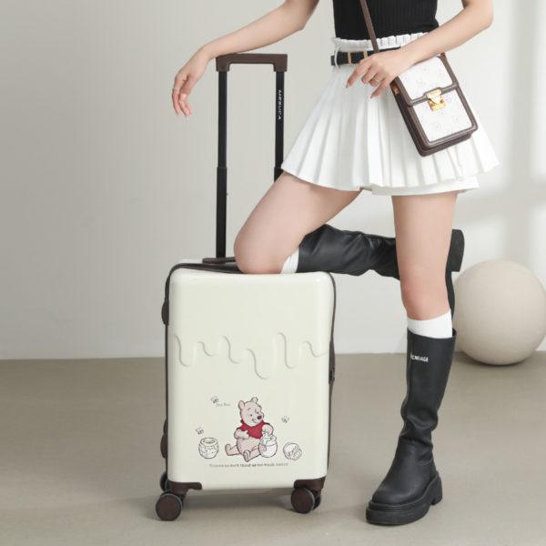 Close-up of a young woman posing with the Winnie the Pooh 24-inch suitcase, showcasing the suitcase design featuring Pooh and honey pots.